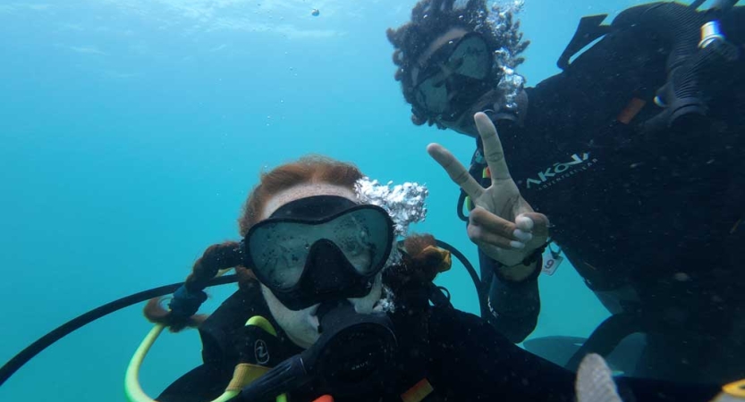 Two people pose for a photo while scuba diving. One of them is giving a peace sign. 